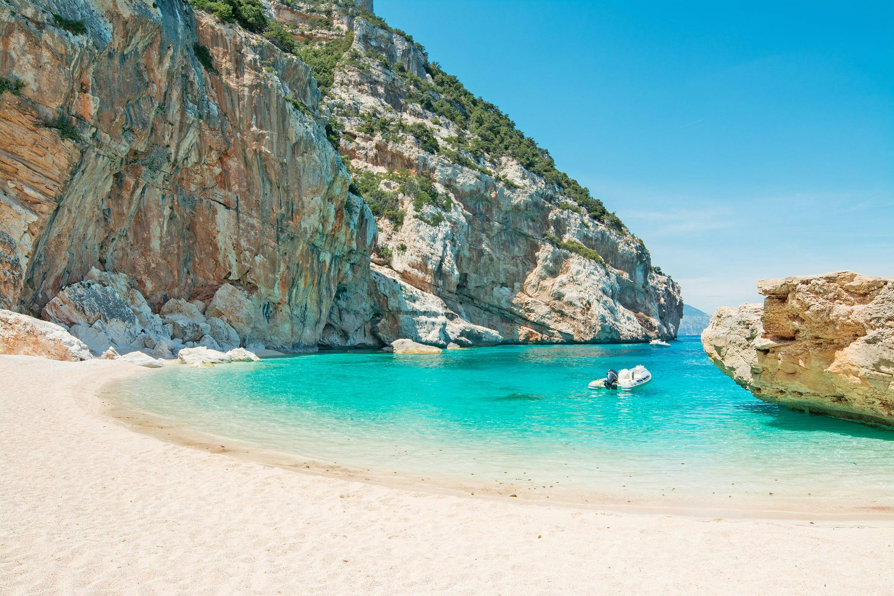 A boat floating on crystal-clear turquoise water near the cliffs of Cala Mariolu.