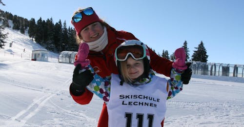 A young girl and her ski instructor from the ski school Skischule Lechner are smiling at the camera during the Kids Ski Lessons for Beginners (5-14 years).