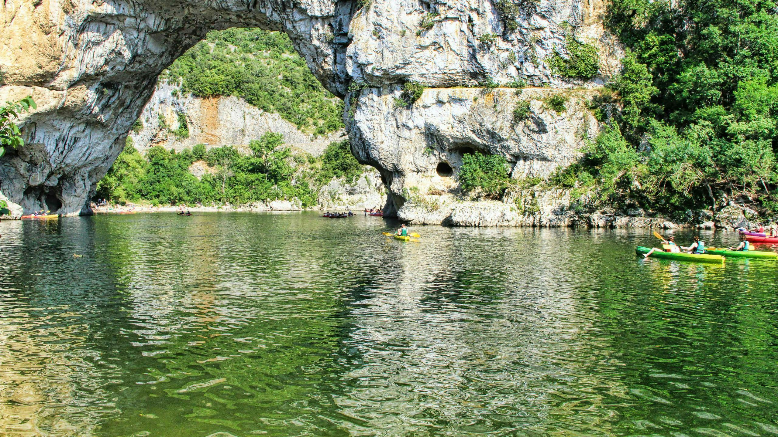 rafting-canyoning-ardeche_SEM-Resort-Hero A group of people is paddling through the Pont-d'Arc while canoeing in Ardèche.