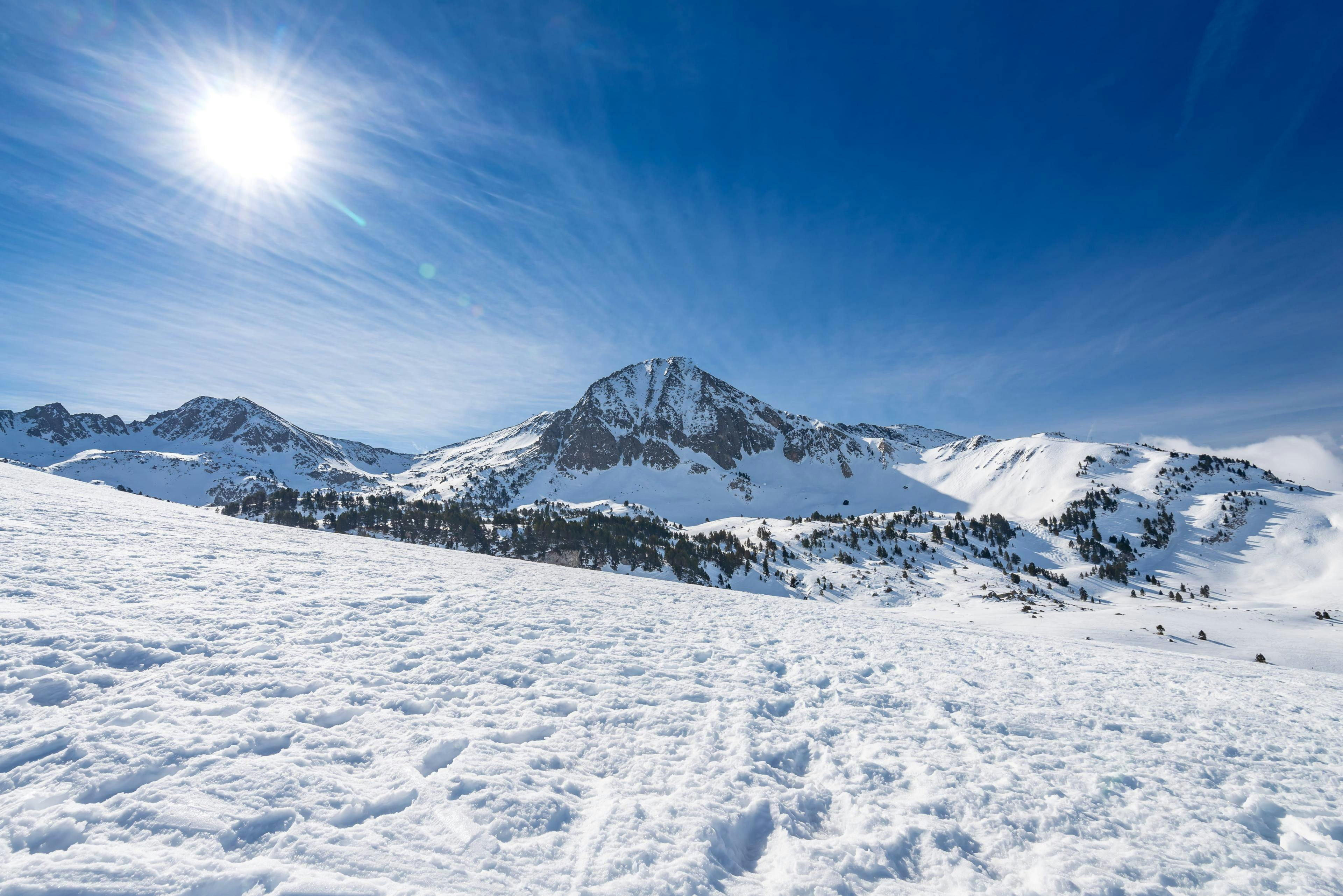 Imagen del sol brillando sobre las montañas nevadas en Baqueira, estación de esquí española done las escuelas de esquí locales ofrecen clases de esquí a los visitantes que quieren aprender a esquiar.