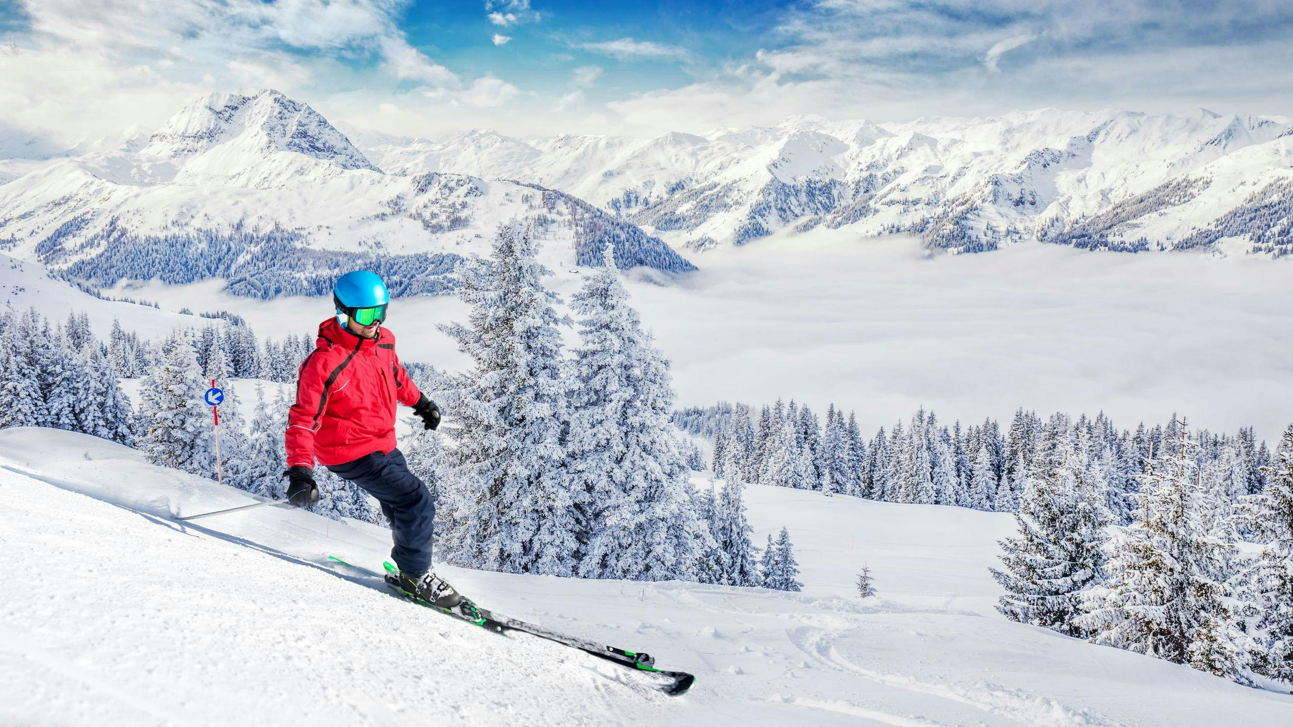 A skier is skiing down a ski slope with fresh powder snow and a stunning view of the surrounding Alps in the Kitzbühel area, where local ski schools offer a variety of ski lessons for anyone who wants to learn to ski.