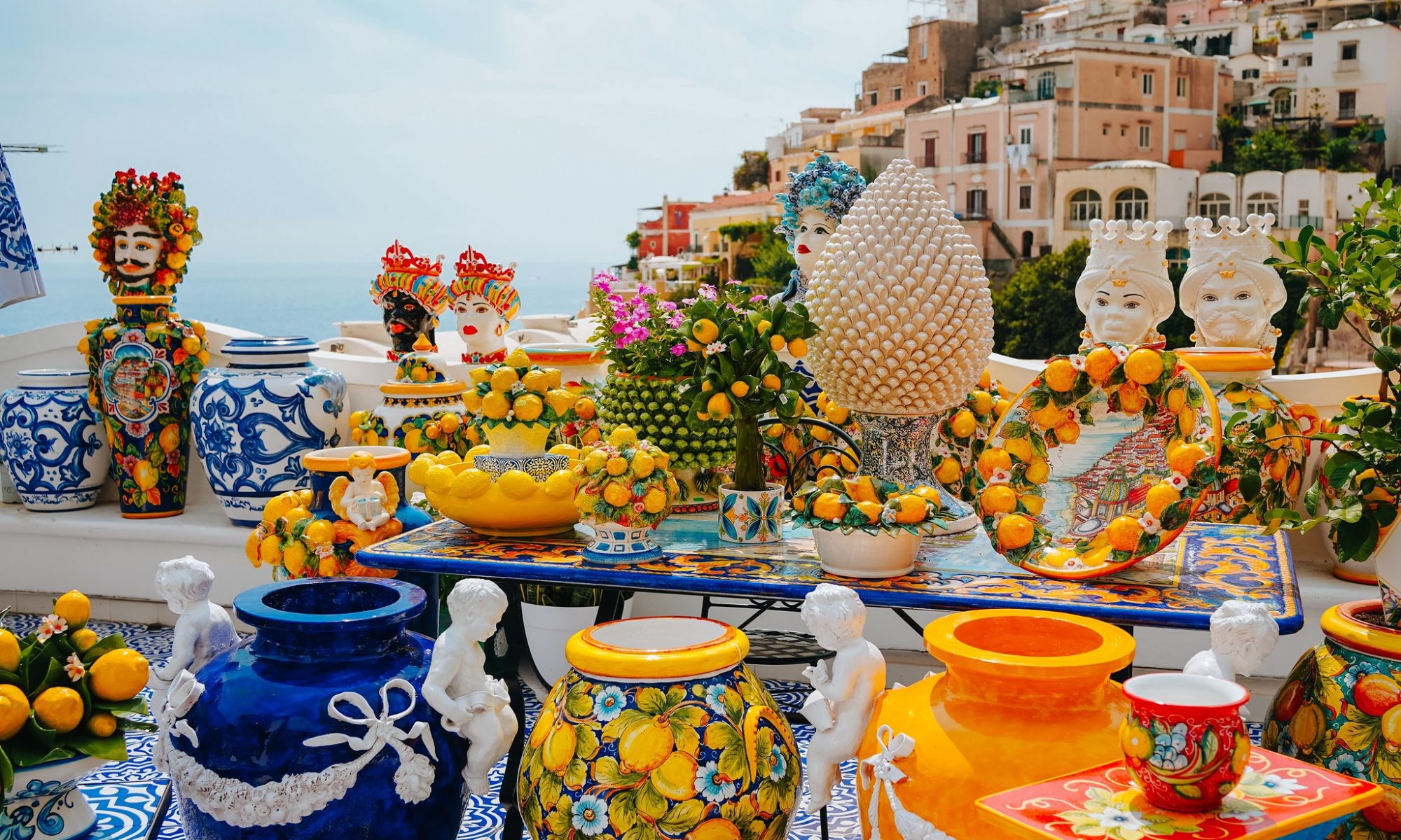 Colourful ceramic pottery and lemon-themed decorations on a terrace overlooking the sea and hillside homes of the Amalfi Coast.